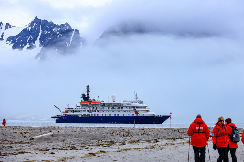 Gäste der Kreuzfahrt kommen von der Spitzbergen Wanderung zurück und gehen an der Küste zu den Schlauchbooten die sie zurück an Bord bringen